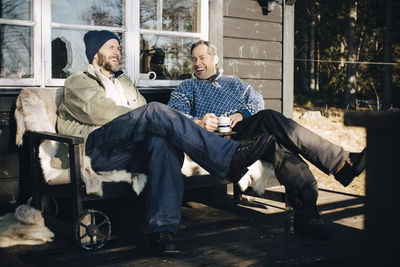 Cheerful mature men talking while having coffee together at porch during winter