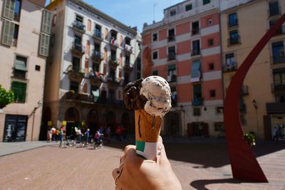 Cropped hand of woman holding ice cream against buildings