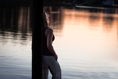 Side view of young woman standing by lake during sunset