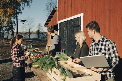 Multi-ethnic farmers arranging organic vegetables on table outside barn