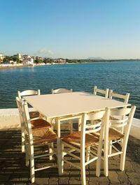 Chairs and table by sea against clear sky