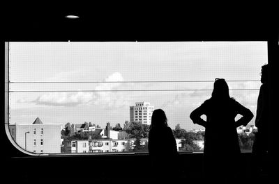 Rear view of silhouette woman standing by window in city