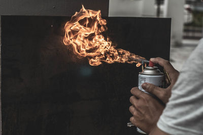 Close-up of man spraying fire on wall with spray bottle