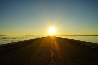 Road amidst bonneville salt flats against clear sky during sunrise