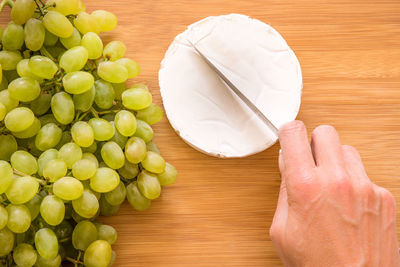 High angle view of hand holding a knife and cutting cheese on table