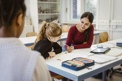 Smiling female teacher explaining schoolgirl sitting at desk in classroom