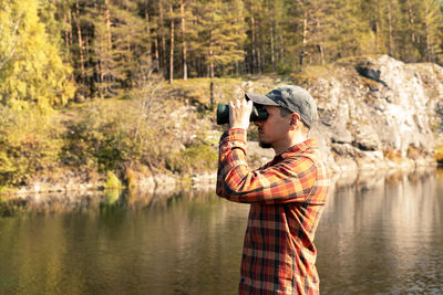 Side view of man photographing while standing against lake