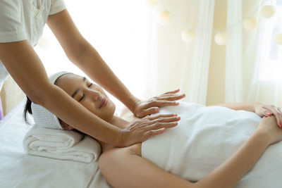 Cropped hands of massage therapist massaging young woman in spa