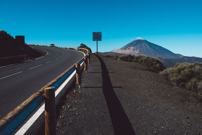 Road passing through mountains against clear blue sky