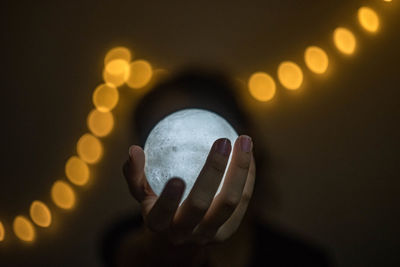 Person holding crystal ball against illuminated lights