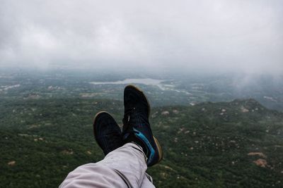Low section of person on mountain against cloudy sky