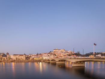 Bridge over river by buildings against clear blue sky