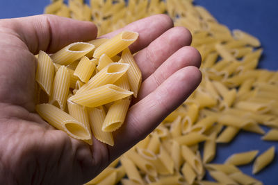 Hand holding dry tubular penne pasta, healthy food background