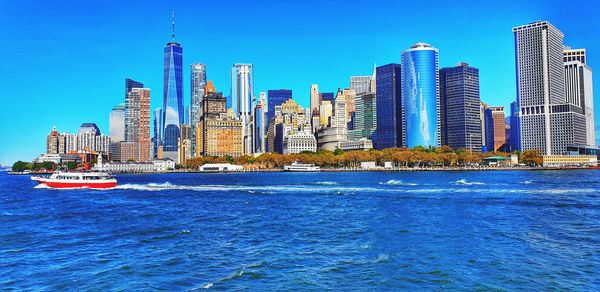 Sea by modern buildings in city against blue sky