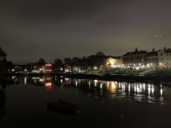 Illuminated buildings by river against sky at night