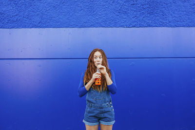 Full length of young woman standing against blue wall