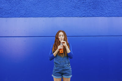 Full length of young woman standing against blue wall
