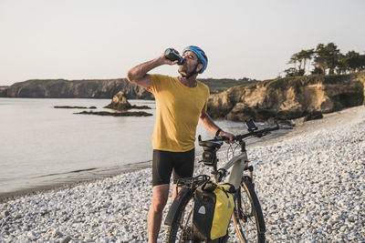 Mature man with bicycle drinking water at beach