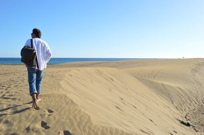 Rear view full length of man walking on sand against clear sky