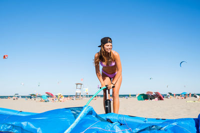 Low angle view of woman sitting on beach against clear blue sky