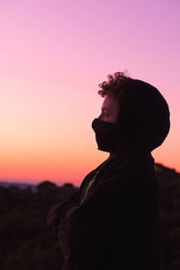 Side view of boy wearing flu mask standing against sky at dusk