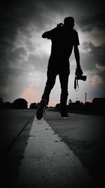 Rear view of silhouette man skateboarding on street against sky
