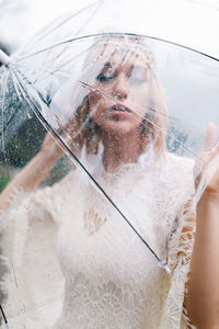 A young woman in a white lace wedding dress stands in the rain among the sea and mountains