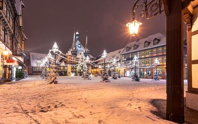 Illuminated street amidst buildings against sky during winter at night