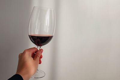 Woman's hand holding a glass of red wine over the white wall. wine tasting