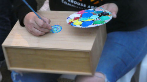 High angle view of woman holding paintbrush making aboriginal dot painting. 