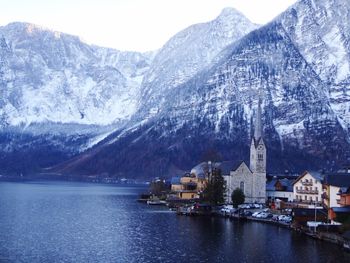 Scenic view of lake by buildings against mountains during winter