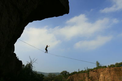 Low angle view of woman slacklining against cloudy sky