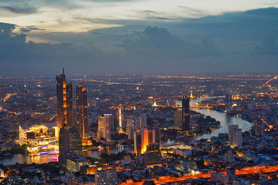 Illuminated buildings in city against cloudy sky