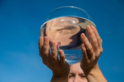 Woman holding round aquarium with goldfish on blue sky background