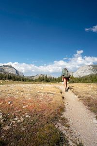 Rear view of hiker walking on trail against sky