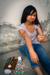 Sad teenage girl with drugs sitting on floor against wall