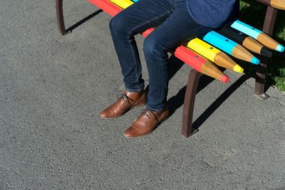 Low section of man sitting on bench during sunny day