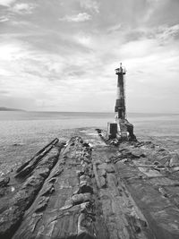 Rock formation and lighthouse by sea against sky