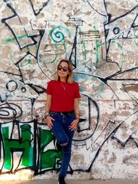 Portrait of young woman standing against graffiti wall