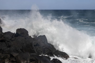 Waves splashing on rocks at shore against sky