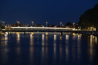 Illuminated buildings by river against sky at night