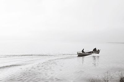 Men sailing boat in lake against clear sky