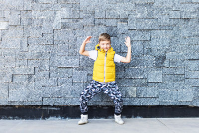 Full length portrait of boy gesturing while standing against stone wall