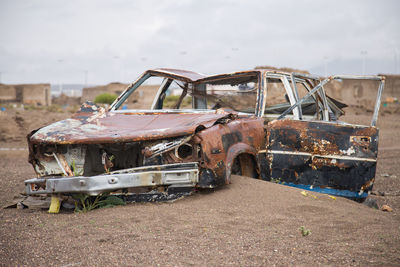 Old abandoned car on field against sky