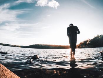 Rear view of man standing in lake against sky