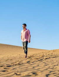 Full length of young woman standing at desert against clear sky