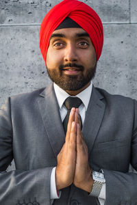 Portrait of smiling businessman wearing turban with clasped hands against wall