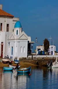 Boats in canal by buildings against clear blue sky