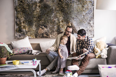 Fathers reading book to daughter while sitting on sofa at home