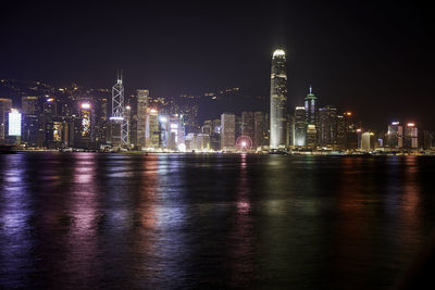 Illuminated buildings by river against sky at night in hong kong